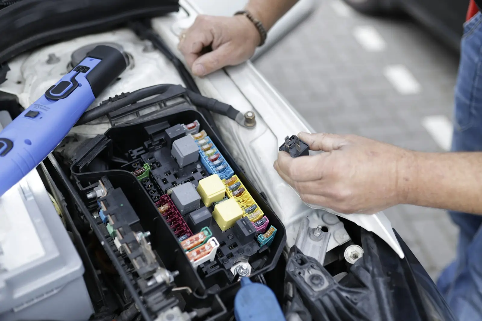 Technician testing fuses and relays in a car fuse box