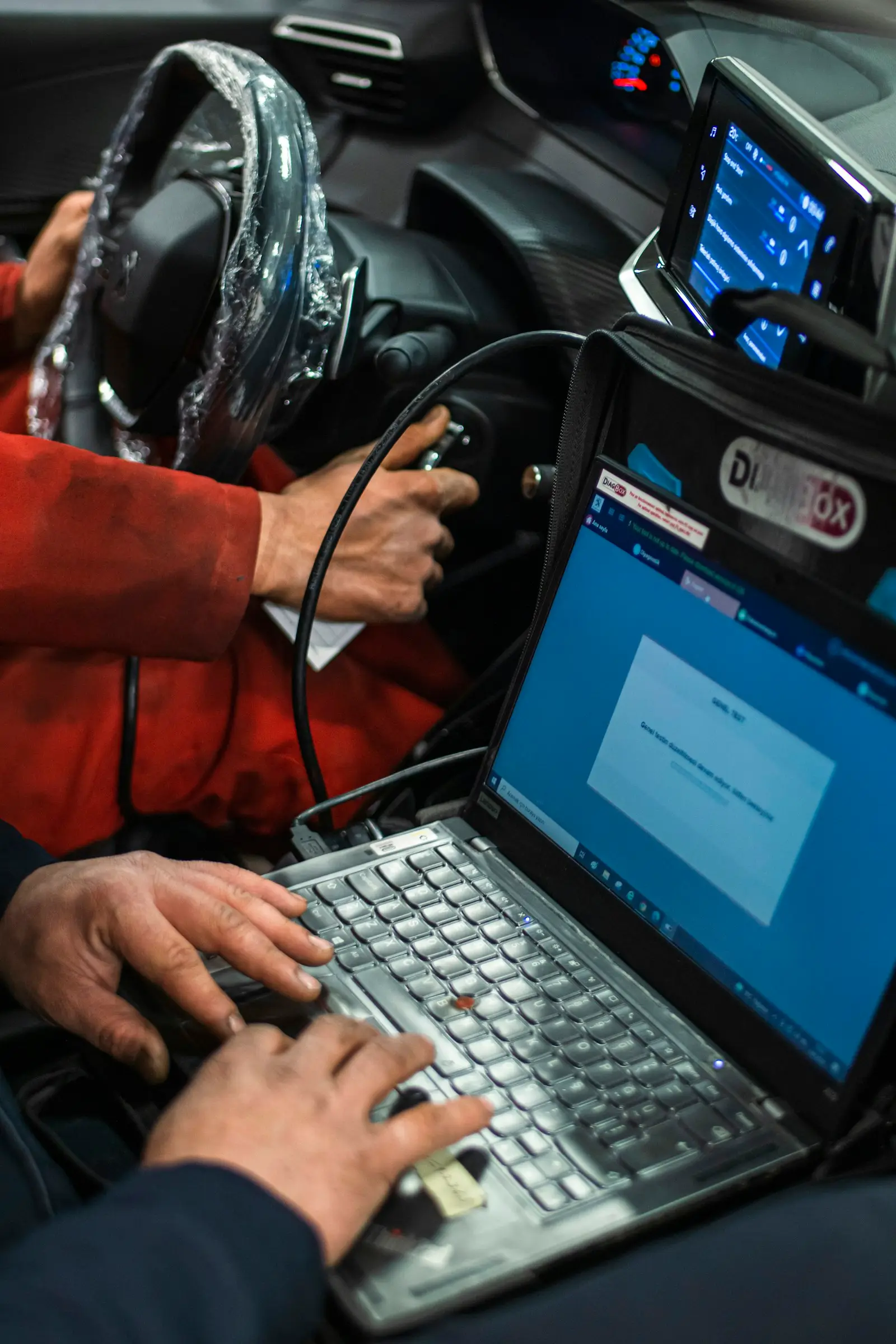 A technician running diagnostics from a laptop connected to the car